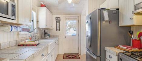 Una cocina compacta con muebles blancos, un refrigerador de acero inoxidable, una estufa a gas y un ventilador de techo.