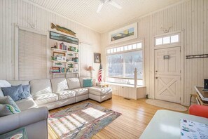 A cozy living room with a sectional sofa, a bookshelf, a small table, and a door with a window. - Historic cozy cottage in Walloon Lake village close to Boyne Mountain skiing! (Walloon Lake)