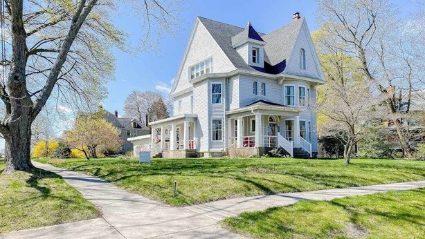 A large, two-story house with a prominent gable roof and a front porch. - Historical dog-friendly home with fenced yard, grill, Ping-Pong, fireplace, & AC (Manistee)