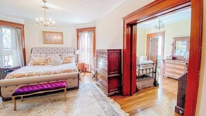 A bedroom with a large bed, a dresser, a bench, and a mirror. - Historical dog-friendly home with fenced yard, grill, Ping-Pong, fireplace, & AC (Manistee)