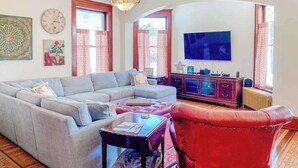 A living room with a sectional sofa, a red leather chair, a television, and a fireplace. - Historical dog-friendly home with fenced yard, grill, Ping-Pong, fireplace, & AC (Manistee)