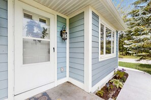 A house with a porch, a window with a frosted glass pane, and a wall-mounted lantern. - Cozy Home Located near Lakes & Trails, large backyard, eV charger & WIFI (Lake Leelanau)