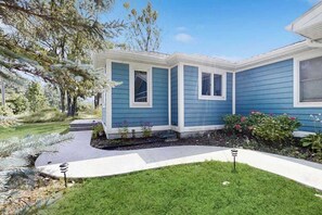 A house with a blue exterior, a front yard with a pathway, and a small garden area. - Cozy Home Located near Lakes & Trails, large backyard, eV charger & WIFI (Lake Leelanau)
