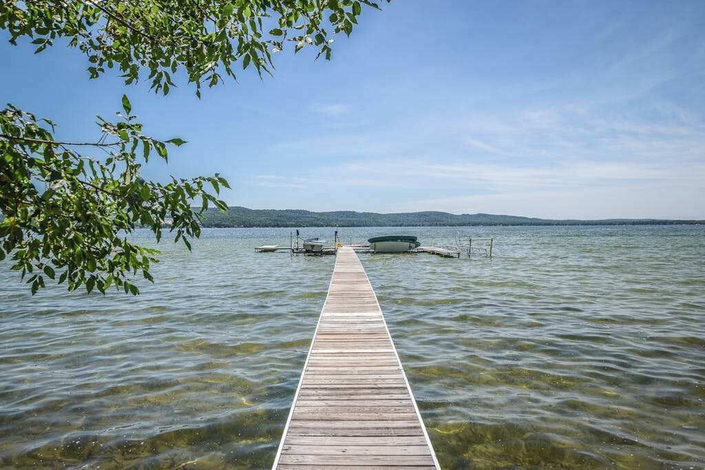 A wooden pier extending into a lake with clear water, surrounded by trees and boats.