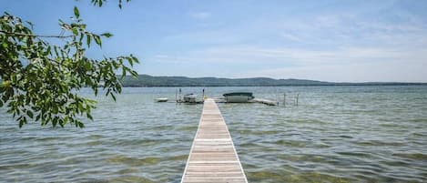 A wooden pier extending into a lake with clear water, surrounded by trees and boats.