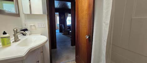 A bathroom with a white sink, mirror, and wooden door leading to a bedroom.
