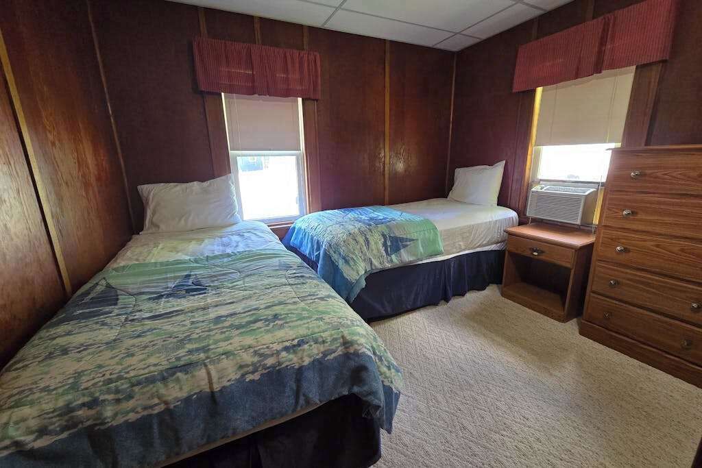 Una habitación con dos camas, un aparador y una ventana con cortinas.