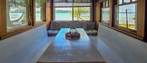 A room with a long table, a sofa, and large windows with a view of a body of water.