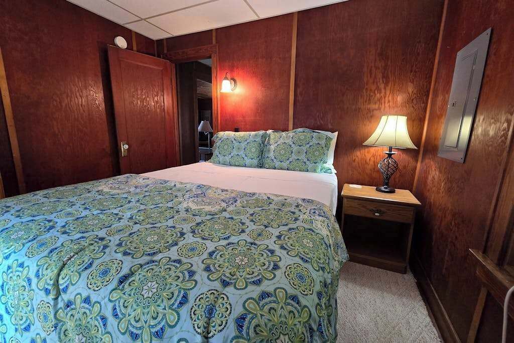Une chambre d’hôtel avec un lit, une table de chevet, une lampe et des panneaux de bois aux murs.