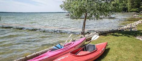 A calm lake with kayaks and a tree by the shore.
