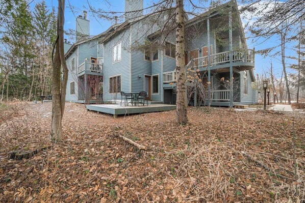 A two-story house with a balcony, surrounded by trees and a leaf-covered ground.