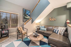A cozy living room with a sofa, armchair, and coffee table, a staircase, and a 'Relax' sign on the wall.