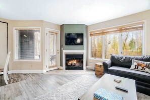 A living room with a fireplace, a flat-screen TV, a sofa, and large windows.