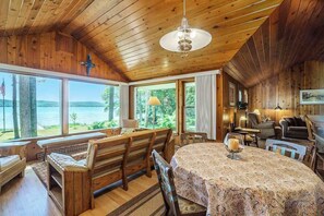 A cabin with a wooden interior, large windows overlooking a lake, a dining table, and a fireplace. - Relaxing lake house w/ firepit, boat mooring, free cable, and full kitchen (Honor)