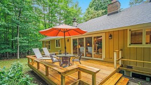 Eine Holzdielen-Terrasse mit Tisch und Stühlen, einem roten Sonnenschirm und einem Wintergarten.