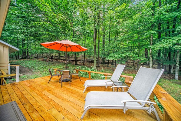 Eine Holzterrasse mit zwei Liegestühlen und einem Tisch, umgeben von einem Wald.