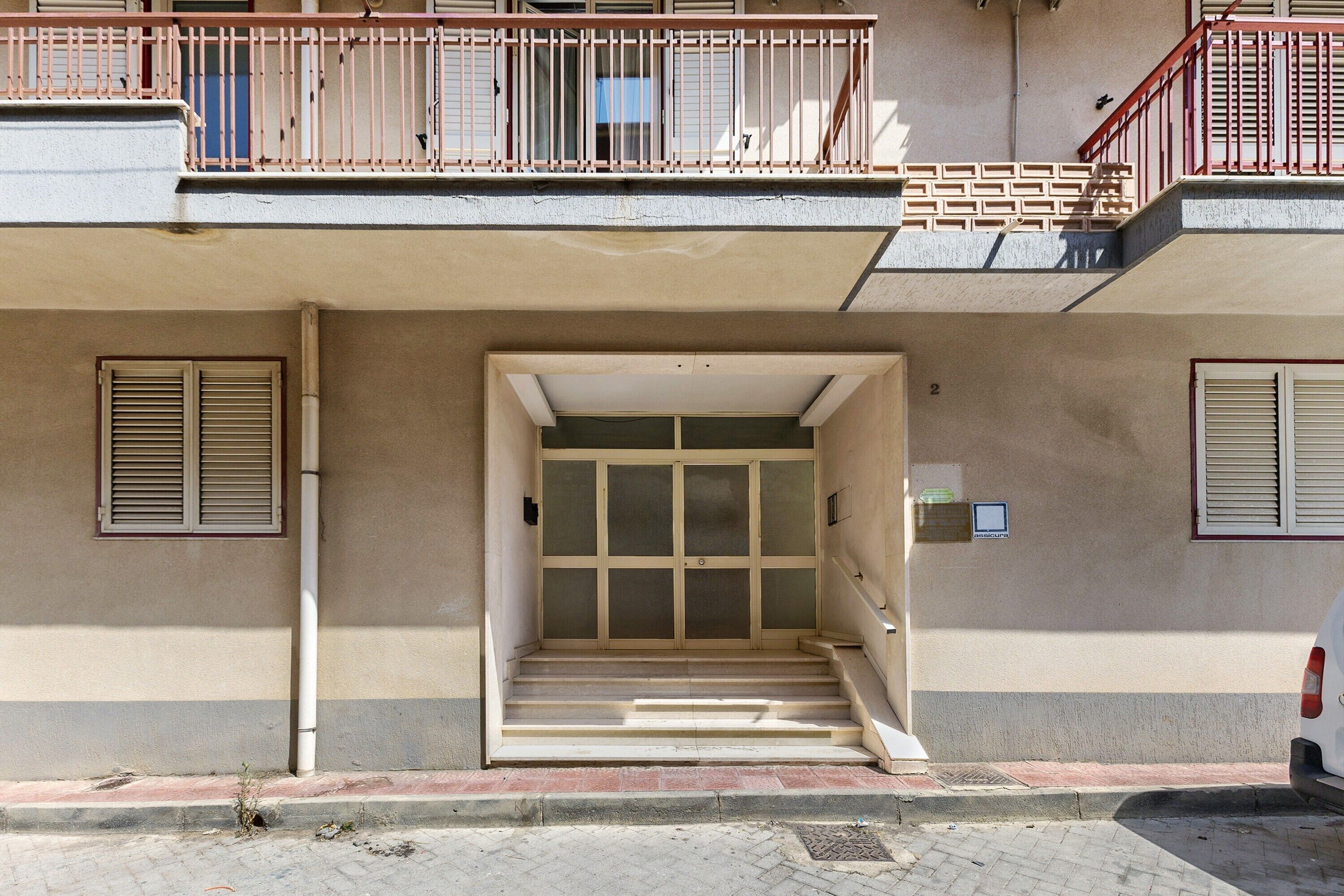 Entrada de un edificio con una escalera que lleva a una puerta con un panel de vidrio.
