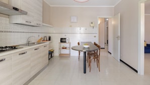 A modern kitchen with a gas stove, microwave, and sink. There's a dining table with chairs and a small shelf with kitchen items. - Apartment "Rina Centro Sicilia" (Pietraperzia)