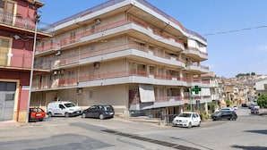 A multi-story residential building with balconies, parked cars, and a street view. - Apartment "Rina Centro Sicilia" (Pietraperzia)