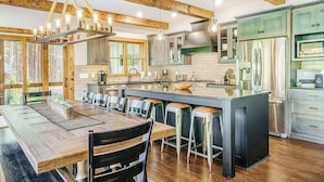 A modern kitchen with wooden beams, a large island, bar stools, and stainless steel appliances. - Expansive dog-friendly home w/ golf course views, and nearby resort amenities (Thompsonville)