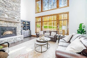 A spacious living area with a stone fireplace, large windows, leather furniture, and a stone wall.
