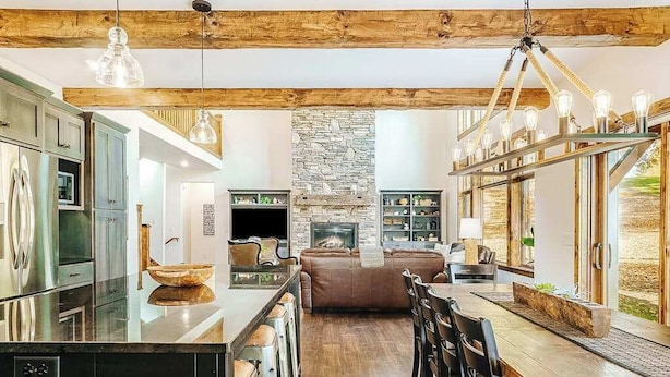 A spacious kitchen with a central island, a stone fireplace, and a dining area with wooden flooring and bar stools. - Expansive dog-friendly home w/ golf course views, and nearby resort amenities (Thompsonville)