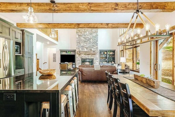 A spacious kitchen with a central island, a stone fireplace, and a dining area with wooden flooring and bar stools.