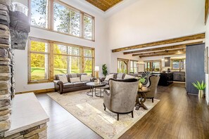 A spacious living area with a stone accent wall, large windows, a fireplace, and a dining area with a view of the outdoors.