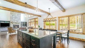 A spacious kitchen with a central island, wooden beams, large windows, and a stone fireplace. - Expansive dog-friendly home w/ golf course views, and nearby resort amenities (Thompsonville)