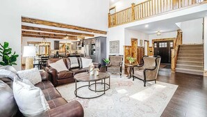 A spacious living area with a high ceiling, wooden beams, a staircase, and a view of the kitchen. - Expansive dog-friendly home w/ golf course views, and nearby resort amenities (Thompsonville)