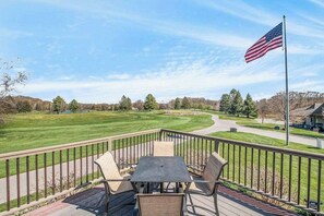 Une terrasse avec une table et des chaises donnant sur un terrain de golf, avec un drapeau américain.