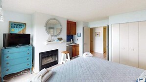Une chambre à coucher avec un lit, un téléviseur posé sur une commode, une cheminée, un miroir et une armoire.