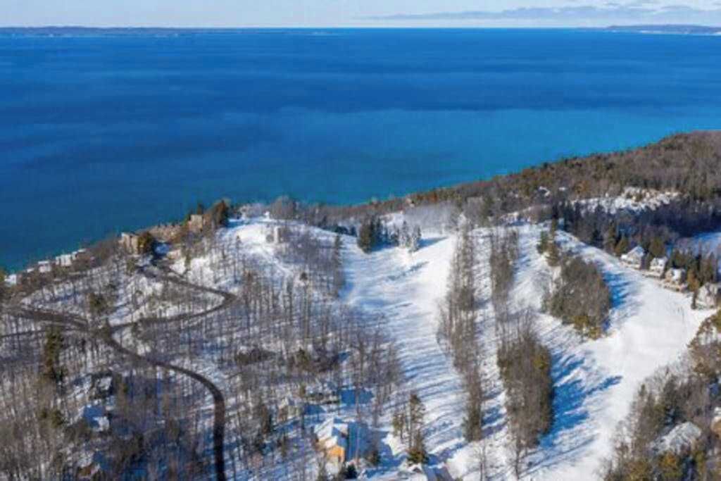 A snow-covered mountain with a ski resort, clear blue sky, and a view of a large body of water.