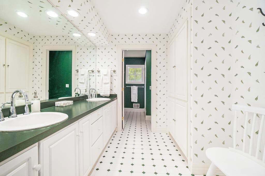 A bathroom with a double sink, white cabinets, a green accent wall, and a patterned floor.
