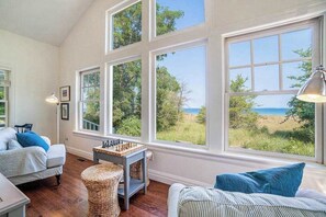 Habitación con ventanas amplias, un tablero de ajedrez, muebles de mimbre y vista a la playa.