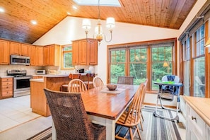 A kitchen with wooden cabinets, a central island, and a dining area with chairs. - Dog-friendly home with gorgeous garden & decks - stroll to town/the lake (Glen Arbor)