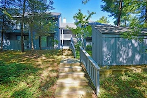 A wooden staircase leading to a house with a porch, surrounded by trees. - Beachfront condo with beach access, fireplace, balcony, washer/dryer & views (Glen Arbor)