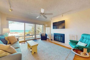 A living room with a sofa, a chair, a fireplace, and a large window with a view. - Beachfront condo with lake views, washer/dryer & fireplace (Glen Arbor)