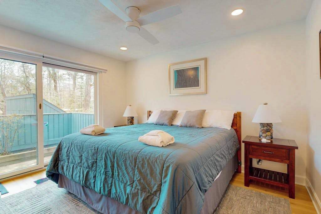 A bedroom with a bed, two bedside tables, a ceiling fan, a window, and a framed picture on the wall.