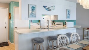 A modern kitchen with a central island, bar stools, and wall-mounted artwork. - Summer Winds 323 - 2 Bedroom Condo (Indian Beach)