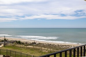 Blick auf einen Strand vom Balkon mit Geländer, ein sandiger Strand und ein klarer Himmel.