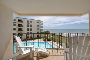 Ein Balkon mit Pool, weißen Stühlen und Blick auf das Meer und ein Gebäude.