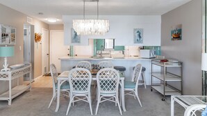 A modern kitchen with a central island, white chairs, and a chandelier. - Summer Winds 323 - 2 Bedroom Condo (Indian Beach)