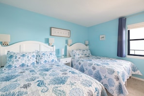 A bedroom with two beds, a window with curtains, and a wall-mounted picture. - Summer Winds 323 - 2 Bedroom Condo (Indian Beach)
