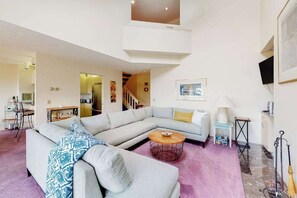 Ein modernes Wohnzimmer mit einer Eckcouch, einem Couchtisch, einer Lampe und einer Treppe, die in einen oberen Bereich führt.