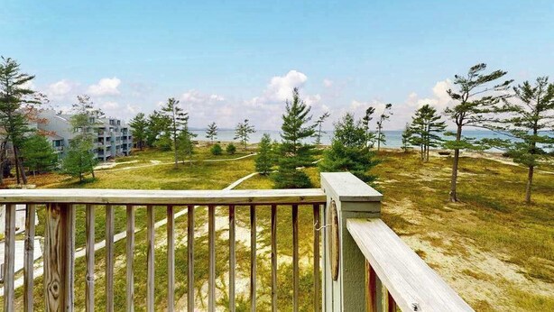 Una terraza de madera con vistas a un área verde, árboles y edificios al fondo.