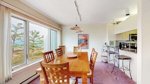 Un área de comedor con una mesa y sillas de madera, un cuadro en la pared y vistas al exterior a través de amplios ventanales.
