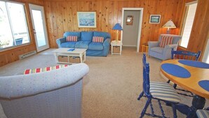 Ein gemütliches Wohnzimmer mit einem blauen Sofa, einem Esstisch mit blauen Stühlen und einem gemusterten Sessel.