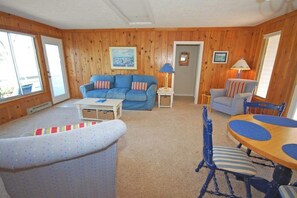 A cozy living room with a blue sofa, a dining table with blue chairs, and a patterned armchair. - Lakefront cottage with a deck, grill, firepit, dock & partial AC (Glen Arbor)