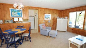 Ein Zimmer mit Holzwänden, einem Esstisch, Stühlen, einer Couch, einem kleinen Hocker, einer Lampe und einem Fenster mit Blick.